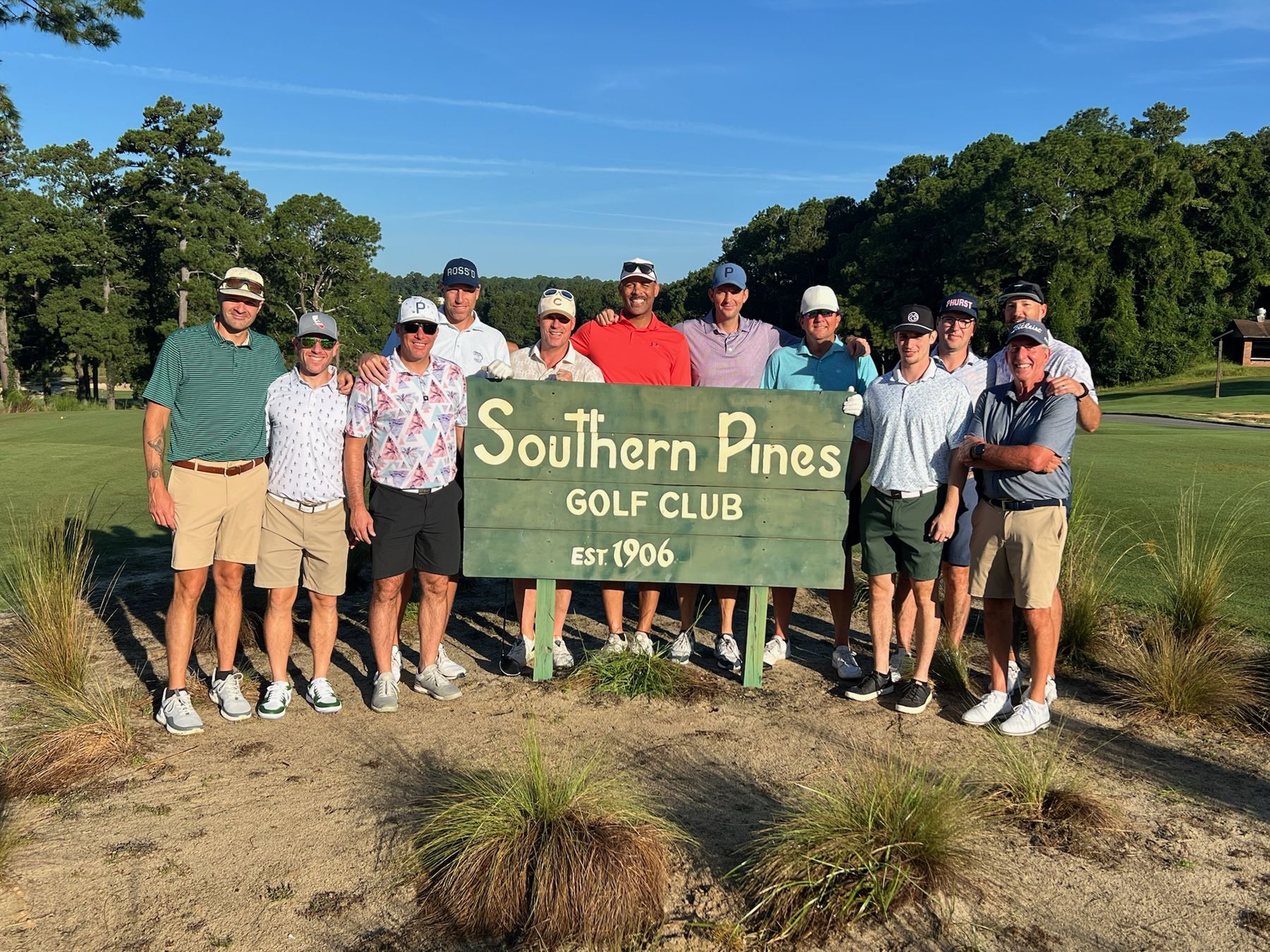 A group of golfers standing behind the Southern Pines Golf Club sign